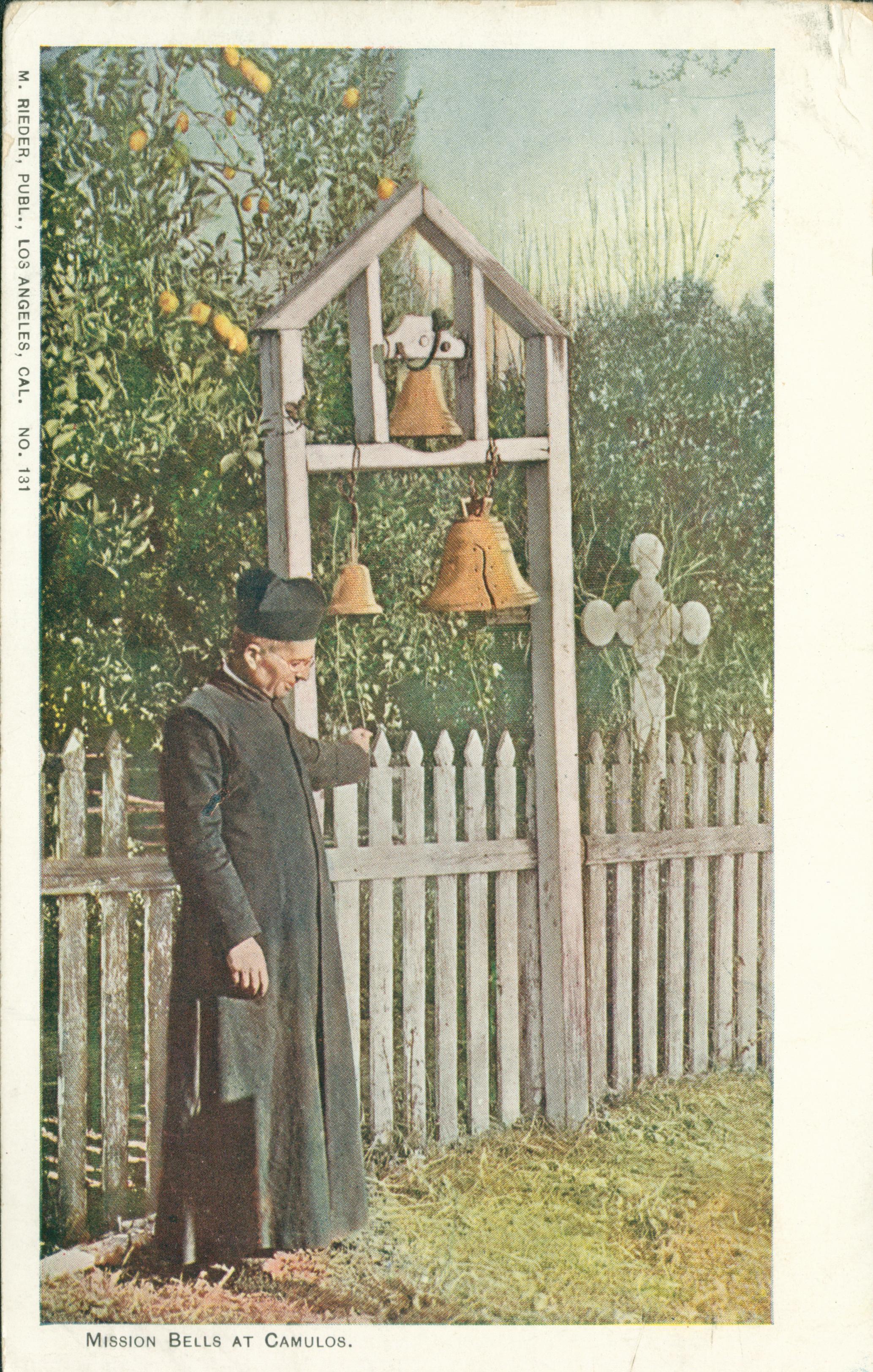 Shows a priest standing next to a wooden structure upon which three bells are hung